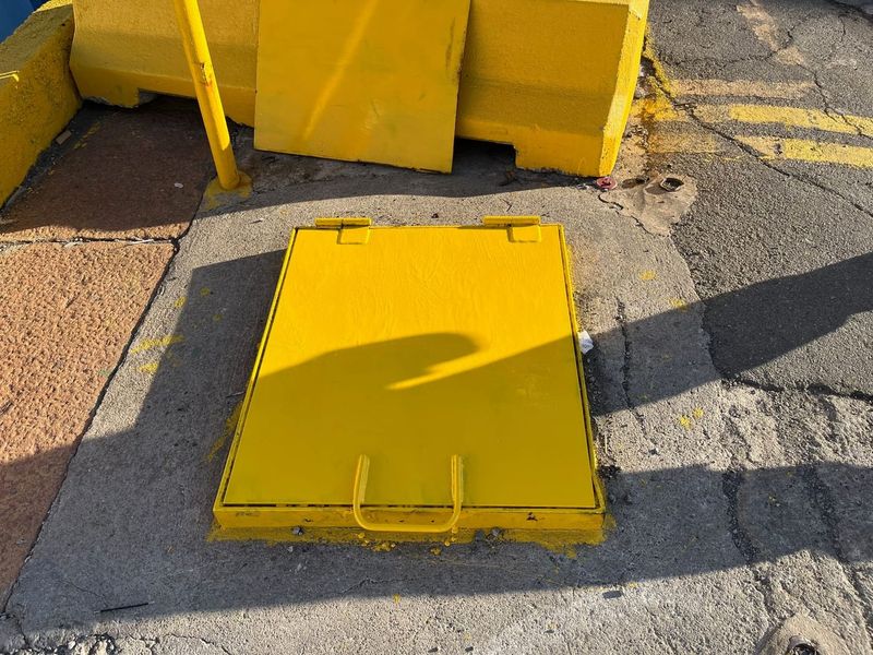 Portello di botola verniciato di giallo, chiuso a filo del piano della banchina