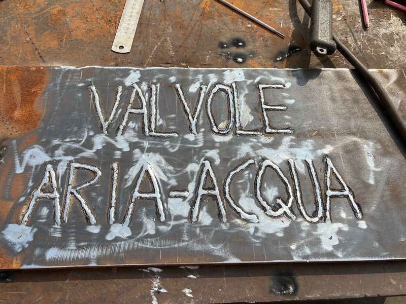 Lamiera con la scritta VALVOLE ARIA-ACQUA tracciata a cordone di saldatura, sul banco