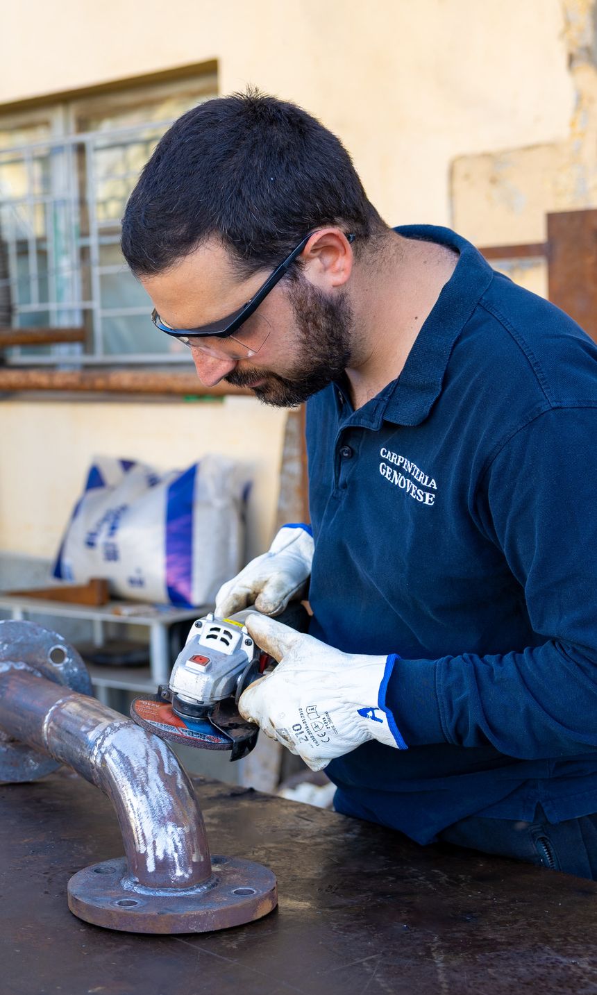 Saldatore al banco che rifinisce con la smerigliatrice il cordone di una curva flangiata