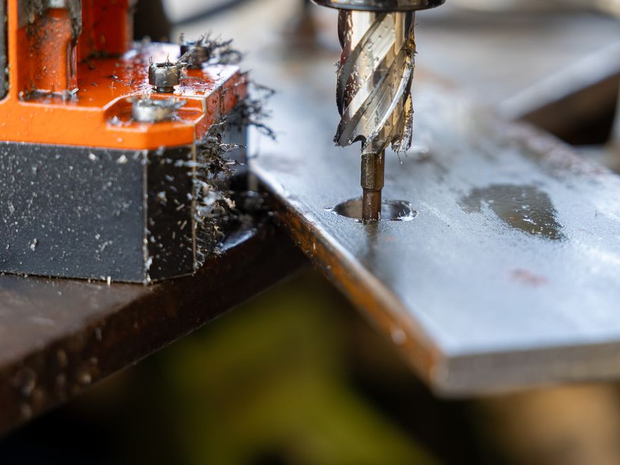 Fresa a tazza del trapano magnetico che fora una piastra di ferro, trucioli sul banco
